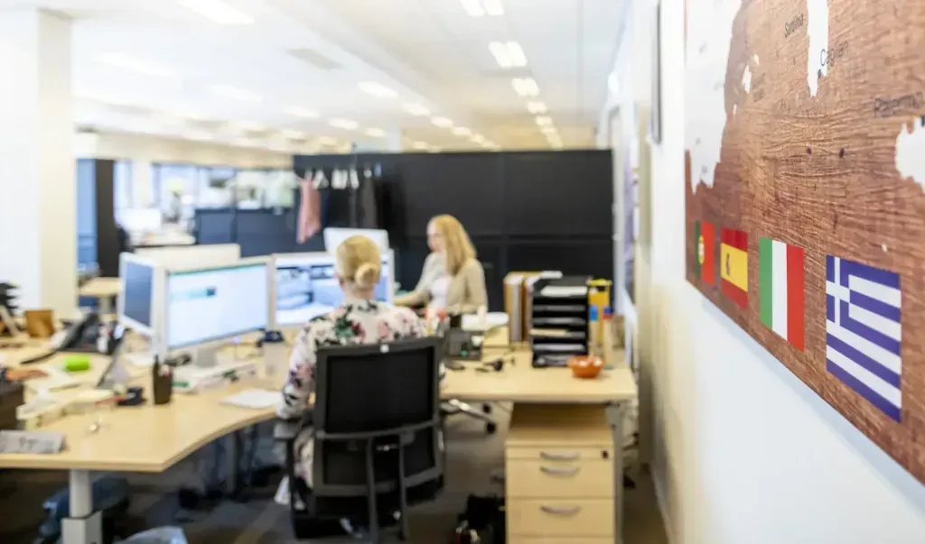 Twee medewerkers aan het werk op het kantoor van Kaemingk, bij een wandkaart met vlaggen